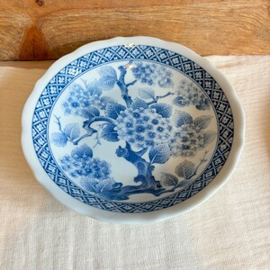 May include: A white ceramic bowl with a blue and white floral design. The bowl has a scalloped edge and a blue and white geometric pattern around the rim.