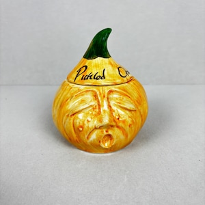 May include: A ceramic onion-shaped jar with a face, in yellow with a green stem. The jar is labelled "Pickled Onions" in black script. The face has closed eyes and a surprised expression.