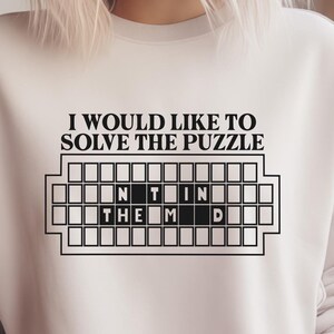 May include: White sweatshirt with black text that reads "I would like to solve the puzzle" and a black and white image of a crossword puzzle with the words "in the mind" filled in.