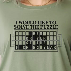 May include: A green t-shirt with the text "I would like to solve the puzzle" and a crossword puzzle with the words "BER", "DRIVER", "OF THE", "FCKING YEAR".