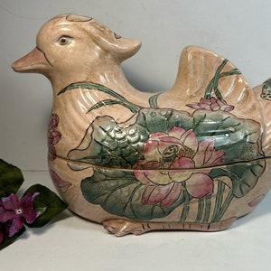 May include: A ceramic duck-shaped serving dish with a pink and green floral design. The dish is decorated with lotus flowers and leaves.