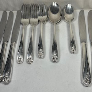 May include: A collection of silver-toned flatware including three dinner knives, three forks, one large spoon, one small spoon, and three additional dinner knives. Each piece features a floral embossed pattern on the handle base and a polished finish.