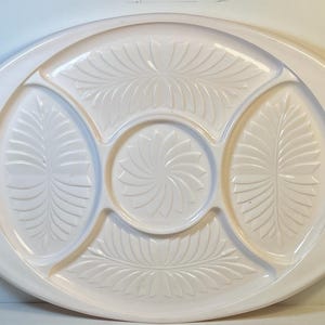 May include: A white oval serving tray with four sections. The tray has two handles and a decorative floral design.