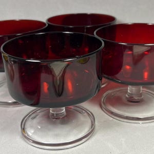May include: Four vintage ruby red glass dessert bowls. Each bowl has a rounded, wide rim and sits atop a clear, circular base. The bowls are made of a deep red glass, and the stems are clear.
