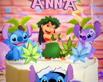 May include: A white cake decorated with a blue Stitch character from the Disney movie Lilo & Stitch. The cake also features a pink and purple "ANNA" name topper, a green lei, and a pink number "6" topper.