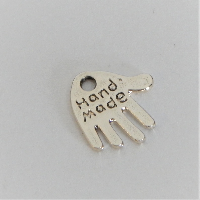 May include: Silver hand charm with the word "Hand Made" engraved on it.