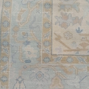Puede incluir: Un primer plano de una alfombra de color azul claro y beige con un diseño floral sutil. La alfombra tiene una superficie suave y texturizada y un aspecto descolorido y vintage.