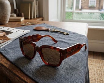 May include: Tortoiseshell-patterned sunglasses with a thick, square-shaped frame and dark-tinted lenses. The temples feature the Gucci brand name in gold-toned lettering and small metallic star accents near the hinges on the front frame.