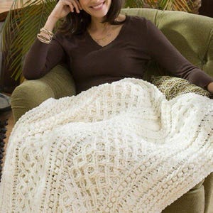 May include: A white crocheted throw blanket with a textured pattern. The blanket is draped over a green armchair.