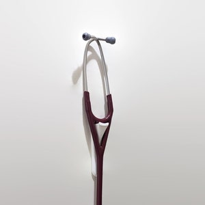 May include: A red and silver stethoscope hanging on a white wall.