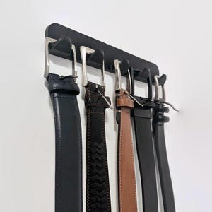 May include: A black belt rack with five leather belts hanging on it. The belts are in various shades of brown and black.