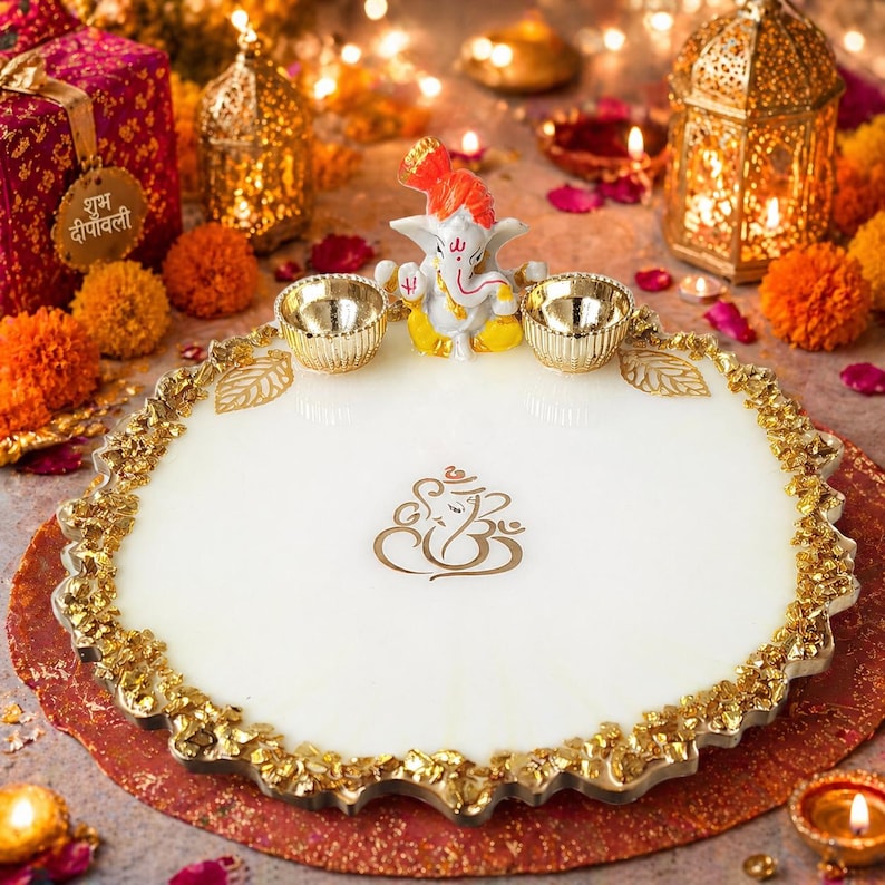 A circular white decorative tray featuring a golden Ganesha emblem sticker in the centre and a textured gold stones border. The tray includes two small gold-coloured bowls and a small Ganesha figurine positioned at the top edge of the tray.