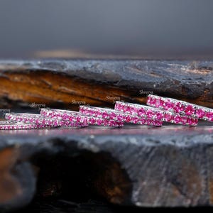 Peut inclure: Un ensemble de six alliances éternelles en argent avec des pierres précieuses roses. Les alliances sont empilées les unes sur les autres, la plus grande en bas et la plus petite en haut.