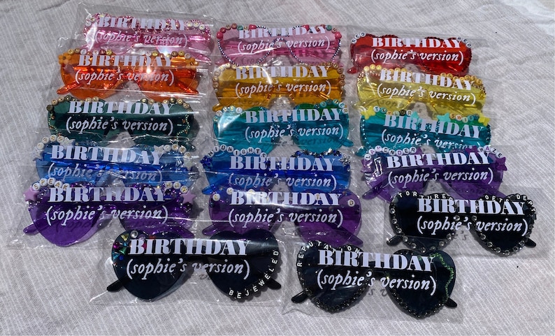 May include: A set of 12 rainbow-colored heart-shaped sunglasses with rhinestones and the text "BIRTHDAY (sophie's version)" on each pair.