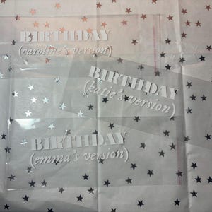 May include: Three clear plastic bags with white text that reads "BIRTHDAY (caroline's version)", "BIRTHDAY (katie's version)", and "BIRTHDAY (emma's version)". The bags are on a white background with silver glitter stars.