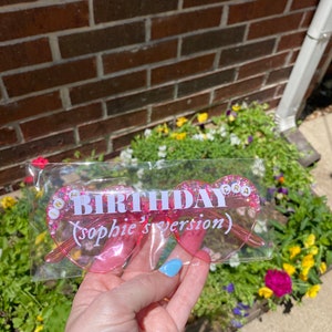 May include: Pink heart-shaped glasses with glitter and the text "Birthday (Sophie's version)" in white letters.