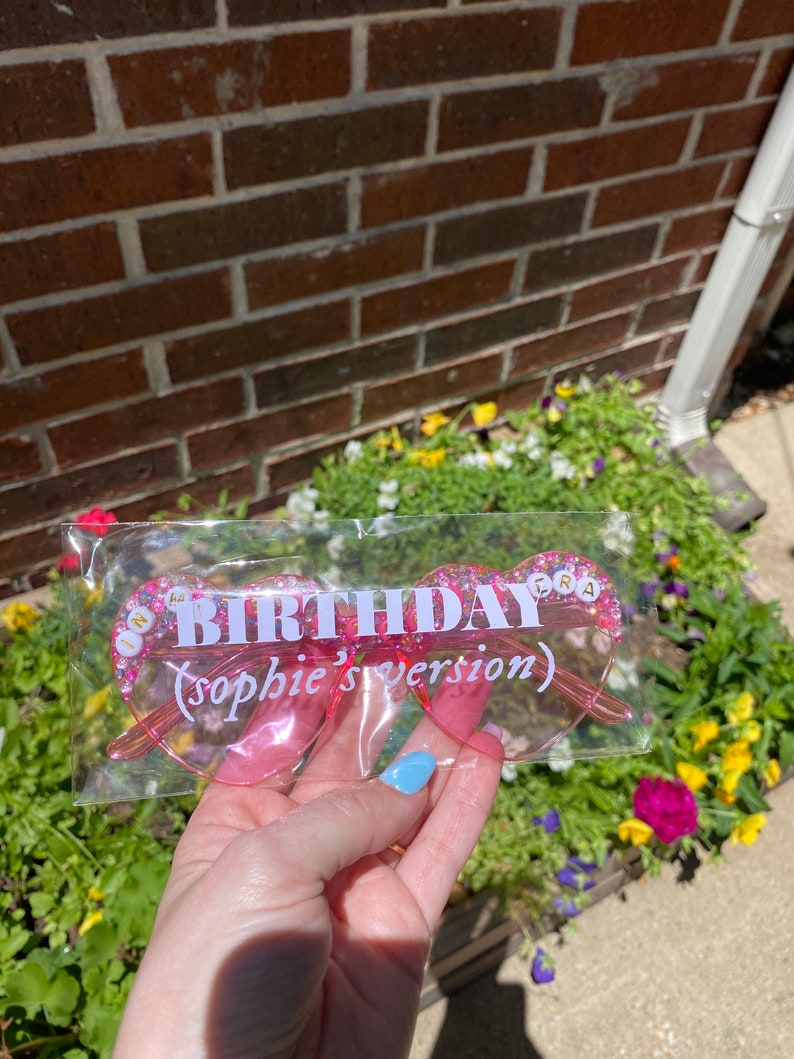 May include: Pink heart-shaped glasses with glitter and the text "Birthday (Sophie's version)" in white letters.