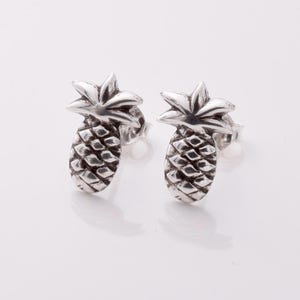 May include: A pair of silver pineapple stud earrings. The earrings are small and delicate, and they feature a realistic pineapple design.