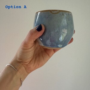 Peut inclure: Une tasse en céramique bleu clair avec un bord brun. La tasse est légèrement irisée et a une forme arrondie.