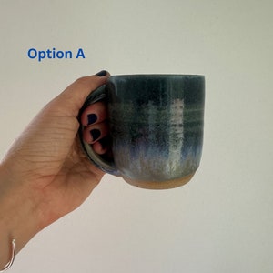 Könnte beinhalten: Eine blaue und grüne Keramiktasse mit einem weißen Streifen. Die Tasse hat eine gesprenkelte Glasur und einen leicht unebenen Rand.