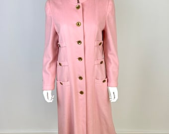May include: A long, pink coat with a mandarin collar and gold buttons. The coat has pockets on the front and is made of a soft, smooth fabric.