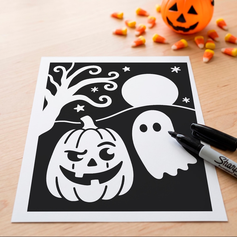 May include: A black and white Halloween-themed coloring sheet featuring a jack-o'-lantern with a mischievous expression, a ghost, a bare tree, a full moon, and stars. A black permanent marker with its cap removed lies on the paper.