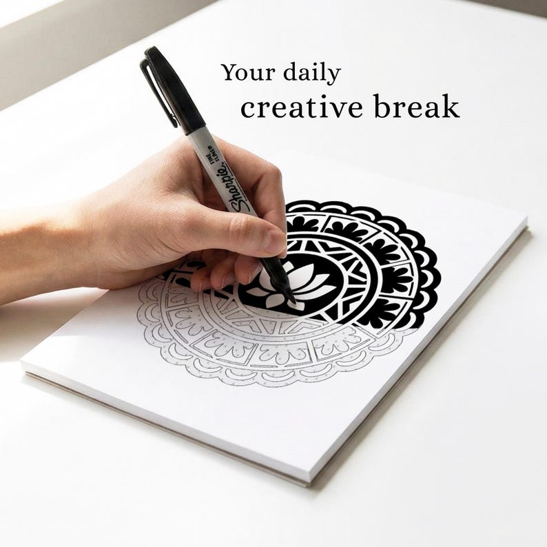 May include: A black Sharpie pen is used to color a black and white mandala design on a white notepad. The text "Your daily creative break" is displayed above the notepad.