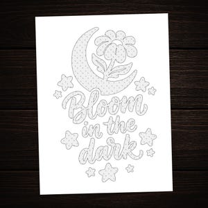 May include: A white coloring page featuring a black line art illustration of a crescent moon, a flower, and several stars. The text "Bloom in the dark" is written in the center in a cursive script font. The entire design has a subtle dot pattern.