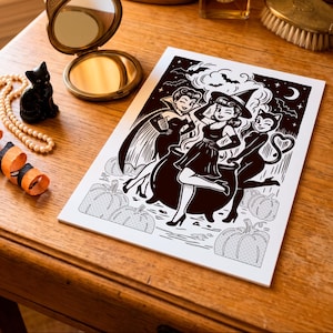May include: A rectangular white print featuring a black ink illustration of three figures, including a witch with a cauldron, a vampire, and a cat-like character, surrounded by pumpkins, bats, and a crescent moon against a starry night sky.