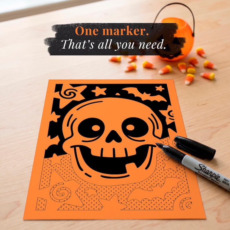 May include: A rectangular coloring sheet featuring a large central skull graphic surrounded by stars and bats. The top portion is filled in with black ink, while the bottom half shows outlines and dot patterns. A black Sharpie marker rests on the paper.