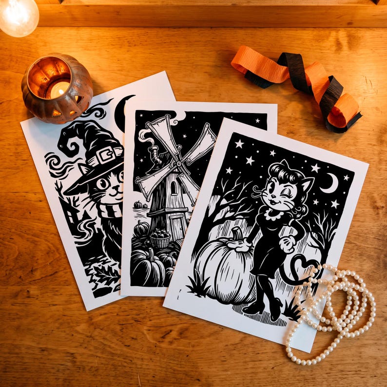 May include: Three rectangular white paper prints featuring black ink illustrations. One print shows a cat wearing a witch hat, another depicts a windmill with pumpkins, and the third displays a cat character standing next to a large pumpkin.