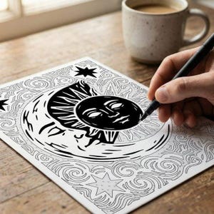 May include: A black and white line art illustration on paper featuring a stylized sun and crescent moon with facial features, surrounded by swirling patterns and stars. A black pen is positioned on the paper, filling in the dark sun design.