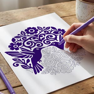 May include: A person is coloring a hummingbird design on white paper with a purple marker. The design features a hummingbird, flowers, and swirling patterns in a deep purple color. A ceramic mug sits in the background.