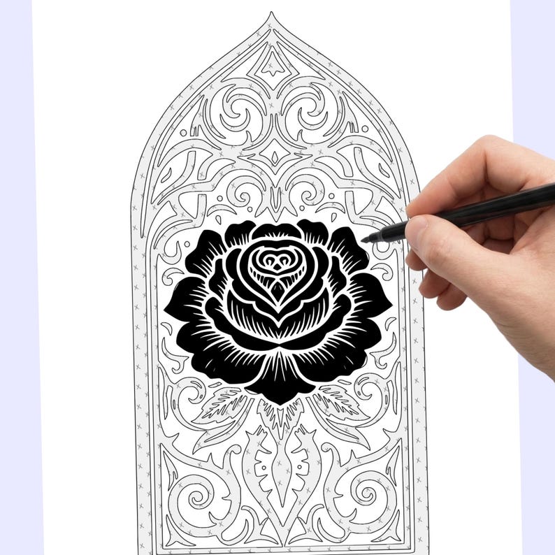 May include: A black rose design within a decorative arched frame, possibly for a coloring book or craft project. The image is in black and white, with a hand holding a pen, suggesting the design is being drawn or colored.