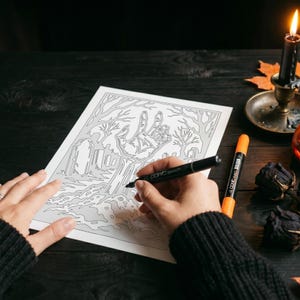 May include: A white sheet of paper featuring a black line art illustration of a hand emerging from a graveyard with tombstones and bare trees. A black Copic Sketch marker is held over the paper, with an orange marker resting nearby.