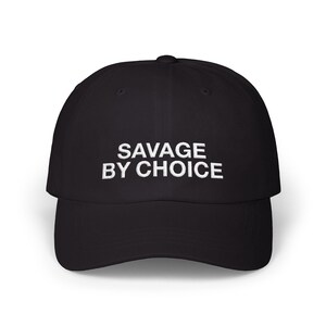 May include: Black baseball cap with the white text "SAVAGE BY CHOICE" embroidered on the front. The cap has a curved brim and a structured fit. A classic, casual accessory.
