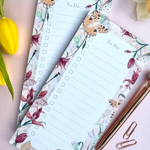 May include: Two floral to-do list pads with a butterfly and dragonfly design. The pads are white with a floral border and have a to-do list heading.