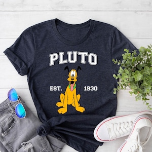 May include: A heather navy blue t-shirt with a cartoon image of Pluto, the Disney dog. The shirt has the text "PLUTO" in white letters above the image and "EST. 1930" in white letters below the image.