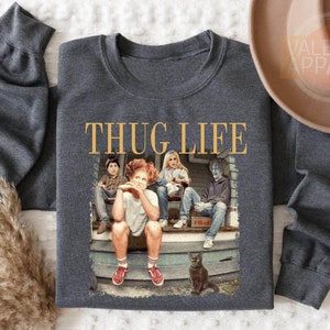 May include: Dark heather gray sweatshirt with the text "THUG LIFE" in gold lettering. The graphic features four characters sitting on a porch with a black cat. The sweatshirt has long sleeves.