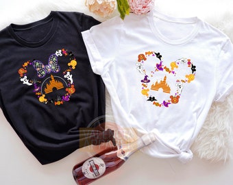 May include: Black and white t-shirts with a Halloween-themed design. The design features a Mickey Mouse head shape filled with ghosts, pumpkins, candy, and a castle. The black shirt has a bow, and the white shirt has a witch hat.