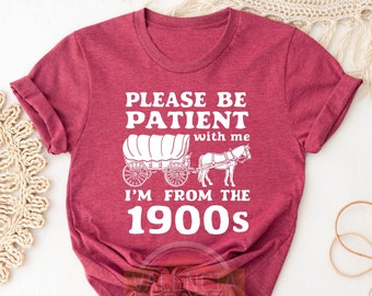 May include: Red t-shirt with white text that reads "Please be patient with me I'm from the 1900s". The text is accompanied by a white silhouette of a horse-drawn wagon.