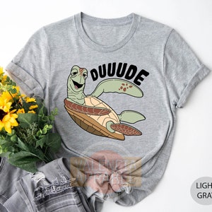 May include: Light gray t-shirt with a cartoon sea turtle wearing a shell and the text "DUUUDE" printed on the front.