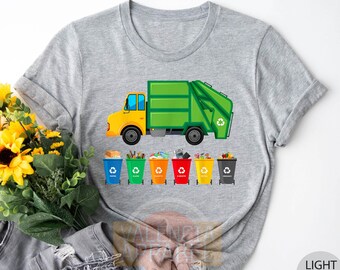 May include: Light gray t-shirt featuring a yellow and green garbage truck illustration. Below the truck are six colorful recycling bins. The bins are filled with various items, including paper, glass, and plastic. The text "LIGHT GRAY" is in a circle on the bottom right.