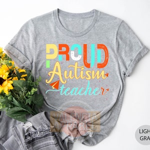 a t - shirt that says proud autism teacher next to a bouquet of sunflower