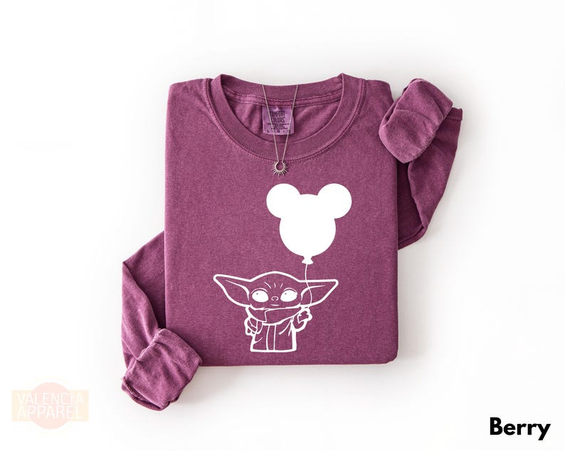 A purple long-sleeved t-shirt with a white graphic design depicting a young alien character holding a balloon.