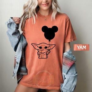 A woman wearing a red t-shirt with a graphic of a cartoon character holding a balloon.