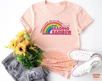 May include: A pink t-shirt with a rainbow and the text "Take a Look, it's in a Book! Reading Rainbow" in red.