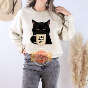 a woman wearing a sweatshirt with a black cat holding a cup of coffee
