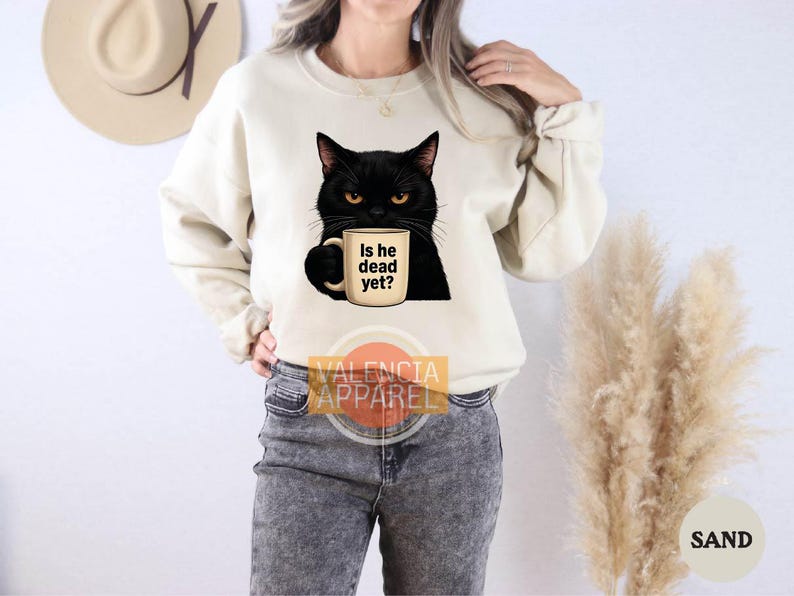 a woman wearing a sweatshirt with a black cat holding a cup of coffee