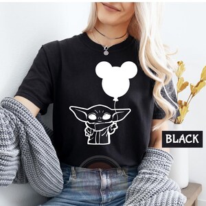 A woman wearing a black t-shirt with a white graphic of a character holding a balloon, along with a necklace.